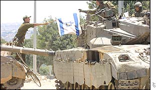 An Israeli soldier passes an Israeli flag from one Merkava tank to another
