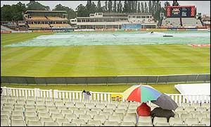 Fans look on under umbrellas as the covers remain on under a heavy shower at the start of the England v Sri Lanka Test match