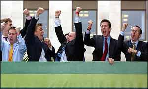 Suited City workers cheers from an office balcony