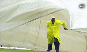 A grounds worker pulls a cover onto the field as rain falls in Grenada