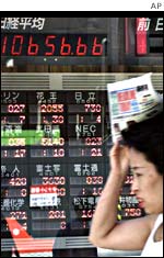 A woman walking past a board showing Tokyo Stock Exchange data