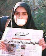 Woman protester with tape over her mouth holds reformist newspaper