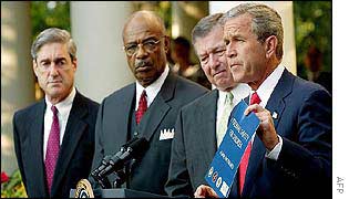 US President George W Bush [r] holds pamphlet as others, including FBI Director Robert Mueller, look on