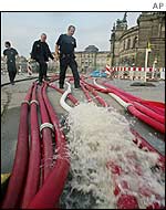 Firefighters walk alongside hoses pumping water out of Zwinger and the Semper opera house, background, in the eastern German city of Dresden