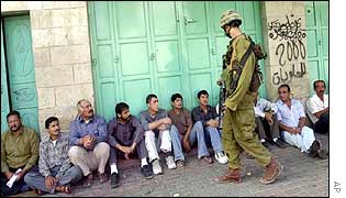 An Israeli soldier watches Palestinian suspects in Hebron