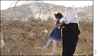 A mother lifts her child through barbed wire placed by Israeli soldiers