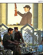 Iraqi workers pedal past huge poster of Saddam Hussein