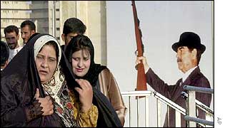 Iraqi women in front of a mural of Saddam Hussein