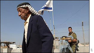 An elderly Palestinian man walks past a checkpoint and a nervous Israeli soldier