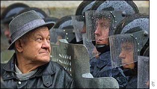Elderly man looks on as riot police block protesters 