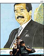 Iraqi family walks past poster of Saddam Hussein