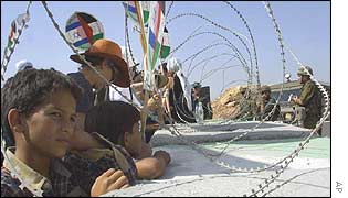 Palestinian children, Israeli and Arab peace activists look across razor wire barrier at Israeli soldiers at West Bank checkpoint