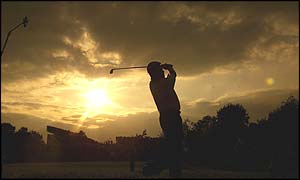 Lee Westwood drives as the sun sets behind him