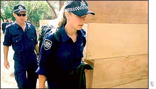 Australian police officers walk near a pile of coffins at a hospital in Denpasar, Bali, Indonesia,
