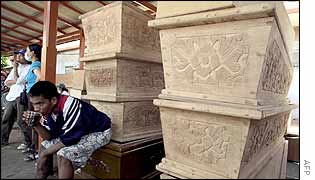 Indonesian man has a drink while sitting on a coffin