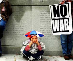 Girl sits by Vietnam War Memorial in Charlotte, North Carolina as a man holds a placard saying 