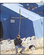 Earth quake victim sits under a wooden cross in a tent camp 