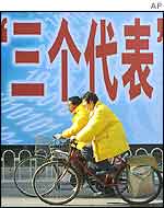 Two cyclists pass a billboard with the characters for the 