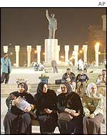 Iraqis sit near a statue of Saddam Hussein