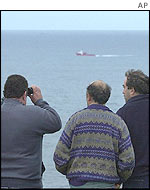 Men look out to sea in search of the huge oil slick heading for the Spanish coast