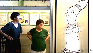 Chinese women walk next to a poster promoting condom use at a sex education exhibit in Beijing 