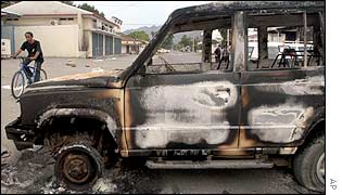 An East Timorese passes by a burnt car belonging to a government official in Dili, 5 Dec. 2002. 