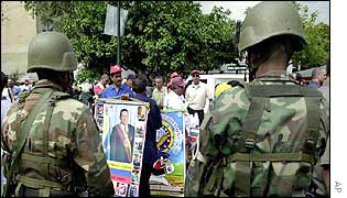 Soldiers look on as a street vendor holds pictures of President Hugo Chavez