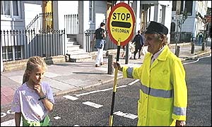 A lollipop lady helps a child across the road