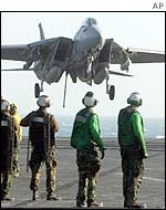 A fighter jet comes in to land, watched by crew on the USS Constellation