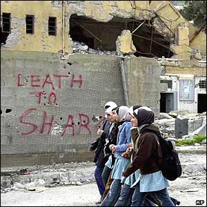 Palestinian students walk past a wall daubed with an anti-Sharon slogan in Nablus
