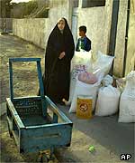 Iraqi woman stands next to her family's food allocation for two months