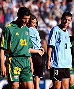 Australia's John Aloisi stands dejected as Alejandro Lembo celebrates Uruguay's qualfiication for the 2002 World Cup