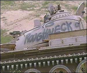 A tank with 'Roughneck' spray-painted on the side lies by the side of the road