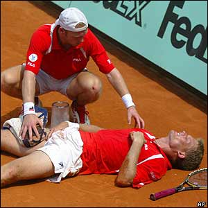 Ferreira, lying on the court, is helped by Schuettler 