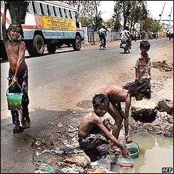 Indian street children fill buckets with water from a puddle on the side of the road in Bhopal