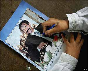 A child defaces a picture of Saddam Hussein
