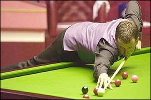 Mark Williams leans over the table to hit a red+
