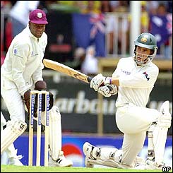 Justin Langer sweeps the ball away as the West Indies' wicketkeeper keeper Ridley Jacobs looks on