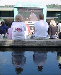 Two spectators sit at the top of Henman Hill watching the action on a giant screen
