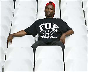 A subduded fan sits in an empty stand wearing a Foe t-shirt