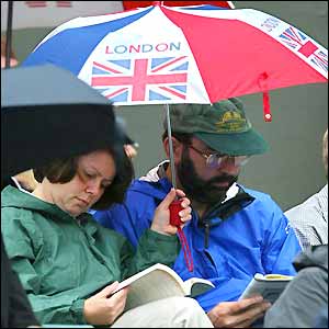 Two fans sit reading books under an umbrella