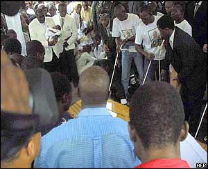 Foe's father, Martin holds his granddaughter in his hands as he watches his son's coffin being lowered into the ground