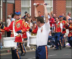 A uniformed bandsman looks on, perhaps in envy at his colleague more sensibly dressed for the weather