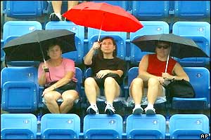Three women sit under umbrellas in the stands at Flushing Meadows