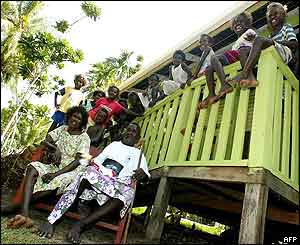 Biuku Gasa (seated R), and his wife Nancy Posa (seated L) sit outside the house built for them by the Kennedy family