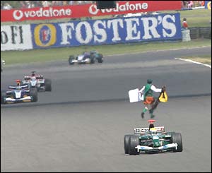 The Formula One field blasts past a protester at the British Grand Prix