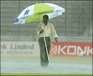 A groundsman walks under an umbrella in the rain in Dhaka