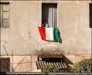 A woman looks out of a window where an Italian flag hangs