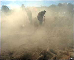 In a mass grave, Iranian relief workers pour dust on the bodies of the people who were killed in the earthquake