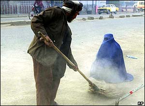 An Afghan man sweeps around a woman begging on the streets of Kabul
